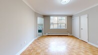 Located at 276 Saint Clair Avenue West in the heart of midtown Toronto, this efficiently designed unit offers a well-organized single-floor layout comprising a living room, kitchen, bathroom, and closet. The living room serves as the central space, showcasing classic parquet wood flooring in a warm honey tone, neutral grey walls, and crisp crown moulding that adds a touch of architectural character. A large window allows natural light to filter in, offering views of the surrounding neighbourhood, while a baseboard heater runs along the wall beneath it. The compact kitchen is thoughtfully appointed with white cabinetry, a marble-patterned countertop, a stainless steel sink, tiled backsplash, and includes a refrigerator and stove. The full bathroom features clean white tile work throughout, including a tiled shower-tub surround, a vanity with mirror, and white tile flooring, creating a bright and functional space. A dedicated closet provides convenient storage. The unit's clean, neutral palette and classic finishes create a practical and comfortable living environment in one of Toronto's well-connected midtown neighbourhoods.