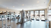 Located at 1001 Belknap St in Superior, Wisconsin, this fitness center offers a spacious, single-floor layout thoughtfully designed to accommodate a comprehensive range of exercise activities. The open floor plan provides ample room to navigate between equipment stations without feeling crowded.

The space is outfitted with a robust selection of Hoist-brand strength machines, including a functional trainer and cable systems, as well as a dedicated free weights area complete with a dumbbell rack and adjustable benches. The cardio zone lines the windowed wall and features multiple treadmills, elliptical trainers, and stair-climbing machines, all positioned to take advantage of natural light streaming in through large windows.

A striking black-and-white athletic mural with bold yellow accents spans a full interior wall, adding visual energy and a motivating ambiance to the space. Large wall-mounted mirrors are strategically placed throughout, enhancing the sense of openness while allowing users to monitor their form. The flooring throughout consists of durable speckled rubber, providing cushioning and safety for all types of workouts.

Recessed ceiling lighting ensures consistent, even illumination across the entire floor. A clearly marked exit door with an accessible entry mat is visible along one wall. The overall design is modern, clean, and functional, creating a professional fitness environment suited for a wide variety of training needs.