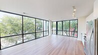 Located in the vibrant Trinidad/Ivy City neighborhood of Washington, DC, this modern single-floor unit at 1326 Florida Ave NE offers a thoughtfully designed layout with clean contemporary finishes throughout. The standout feature of the main living area is its dramatic floor-to-ceiling glass curtain wall spanning two sides of the room, flooding the space with abundant natural light and framing lush treetop views of the surrounding neighborhood. Light-toned hardwood-style flooring runs throughout the living area, contributing to an airy, open ambiance. The bedrooms are well-proportioned, each featuring warm hardwood-style floors and individual windows that bring in natural light and garden views, providing a calm and comfortable retreat. The kitchen is outfitted with sleek white cabinetry, solid-surface countertops, a glass tile backsplash, and stainless steel appliances including an electric range with oven and an over-the-range microwave, delivering a clean, functional workspace. Two bathrooms serve the unit — one featuring a combination tub and shower with white tile surround, and the other a walk-in shower — both finished with large-format stone-look tile flooring and modern floating vanities with white cabinetry. Overall, the space presents a cohesive modern aesthetic defined by natural light, neutral tones, and quality finishes.