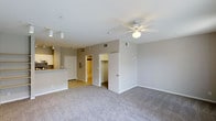 This single-floor residence in Addison offers an open-concept layout that combines the living area and kitchen into one cohesive space. The living area is finished with plush wall-to-wall carpeting and features a ceiling fan with an integrated light fixture, contributing to both comfort and functionality. Neutral gray walls and white trim create a clean, contemporary aesthetic throughout.

Track lighting along the kitchen side provides targeted illumination over the counter space, which includes a raised breakfast bar that visually separates the kitchen from the living area. The kitchen is finished with tile flooring, offering a practical contrast to the carpeted main living space.

Toward the rear of the unit, two open doorways reveal additional rooms. One leads to a bathroom, visible by its light-colored tile and warm lighting, while the other opens to a spacious walk-in closet, providing generous storage. A utility or electrical panel is also accessible along the rear wall. The overall ambiance is bright, neutral, and move-in ready, with a straightforward floor plan designed for efficient everyday living.