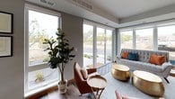 This thoughtfully designed single-floor residence showcases a cohesive modern aesthetic with warm wood tones, neutral palettes, and an abundance of natural light. The open living area is a standout, anchored by expansive floor-to-ceiling windows and a sliding glass door that frame outdoor views and flood the space with daylight. Leather accent chairs, a patterned area rug, and metallic gold accent tables create a stylish, inviting atmosphere.

The kitchen is well-equipped and features flat-front wood cabinetry in warm natural tones, white quartz countertops, a light subway tile backsplash, and a full suite of stainless steel appliances including a gas range, built-in microwave, dishwasher, and french door refrigerator. A central island with bar seating adds both workspace and casual dining functionality, all complemented by durable wood-look flooring.

The primary bedroom offers a serene retreat with large windows, plush carpeting, and sleek wall-mounted lighting. The second bedroom mirrors this calm aesthetic with soft carpet, generous natural light, and contemporary furnishings. Both bathrooms are finished with wood-toned cabinetry, white countertops, and wood-look flooring, with one featuring a full tub-shower combination. The overall design is clean, modern, and cohesive throughout.