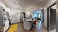 This single-story residence is thoughtfully designed with a contemporary aesthetic, combining functional living spaces with modern finishes throughout. The open-concept layout seamlessly connects the kitchen, dining, and living areas, creating a cohesive and spacious flow ideal for everyday living and entertaining.

The kitchen is a standout feature, equipped with white shaker cabinetry extending to the ceiling, granite countertops, a subway tile backsplash, and a full suite of stainless steel appliances including a refrigerator, electric range, and microwave. A central island with pendant lighting above provides additional prep space and casual seating. Wood-look plank flooring runs throughout the main living areas, adding warmth and continuity.

The living room benefits from natural light through large windows, ceiling fan, and ample space for comfortable furnishings. A dedicated in-unit laundry closet is conveniently accessible from the kitchen area.

Both bedrooms are carpeted and feature ceiling fans. The primary bedroom is generously sized with a window and direct access to an en-suite bathroom, which includes a glass-enclosed walk-in shower, marble-look tile flooring and walls, white cabinetry, and granite countertops. The second bathroom offers a full tub-shower combination with matching marble-look tile.