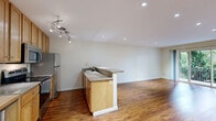 Located in the desirable 94611 zip code of Oakland, CA, this three-bedroom, one-bathroom residence offers a well-organized single-floor layout designed for comfortable everyday living. Rich hardwood flooring runs throughout the home, providing warmth and continuity across every room. The open-plan kitchen and living area forms the heart of the space, where a peninsula with granite countertops separates the kitchen from the living area. The kitchen is equipped with stainless steel appliances—including a refrigerator, range, and microwave—complemented by warm wood cabinetry, track lighting, and a butcher block prep table for added functionality. Recessed lighting illuminates the living area, which opens directly onto a private balcony through sliding glass doors, offering views of surrounding greenery. The three bedrooms are bright and clean, featuring the same hardwood flooring and neutral white walls. The primary bedroom offers a comfortable footprint with access to a dedicated closet. The full bathroom is finished with marble-style tile flooring, a tub-shower combination, brushed nickel fixtures, and a clean, light-filled design accentuated by a frosted window. The overall ambiance is clean, functional, and bright, making it a practical and inviting place to call home.