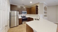 Located at 7521 Windmill Harbor Way in Raleigh, NC, this single-floor home offers a well-designed open-concept layout that seamlessly connects the kitchen and living areas. The kitchen is a standout feature, equipped with rich dark-wood cabinetry, stainless steel appliances including a refrigerator, range, and built-in microwave, complemented by light quartz countertops and a classic white subway tile backsplash. A curved peninsula with an undermount sink adds both functionality and style, while open corner shelving provides additional display or storage space. The living area is bright and spacious, with recessed lighting, crown molding, and a charming built-in arched shelving niche that adds architectural character. Wood-style flooring runs throughout the main living spaces, while the bedrooms feature plush carpeting and ceiling fans with access to natural light through well-placed windows. The bathrooms are appointed with dark wood vanities matching the kitchen aesthetic, light countertops, and tiled tub-and-shower combinations, including a soaking tub in one bathroom. A dedicated laundry area accommodates a full-size washer and dryer with overhead shelving for added convenience. The overall ambiance is clean, neutral, and move-in ready.