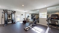 This single-level fitness center is thoughtfully designed to support a comprehensive workout experience. The space is outfitted with durable rubber flooring throughout, providing a safe and functional surface for all types of exercise. Recessed lighting illuminates the room evenly, while multiple windows allow natural light to filter in, creating a bright and energizing environment.

The cardio zone features a treadmill, elliptical trainer, stationary spin bike with an integrated display, and a rowing machine, offering a full range of aerobic options. A multi-functional cable machine serves as the centerpiece of the strength training area, complemented by a full dumbbell rack with weights of varying sizes, a adjustable workout bench, and stability balls. TRX suspension straps and resistance bands provide additional versatility for functional training.

Large wall-mounted mirrors span key sections of the room, visually expanding the space and allowing users to monitor their form during workouts. A wall-mounted flat-screen television adds entertainment value during exercise sessions. Yoga mats and a padded floor mat are available for stretching and floor-based exercises. A wire shelving unit provides organized storage for accessories, and posted fitness center rules ensure a structured, shared-use environment. Multiple entry doors offer convenient access throughout the space.