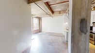 This single-floor loft space showcases a compelling blend of raw industrial character and modern updates throughout. The open main living area immediately draws attention to its exposed concrete ceiling beams, visible ductwork, and original brick accent walls, all of which contribute to an authentic warehouse aesthetic. Polished concrete floors extend throughout the space, adding to its industrial charm while remaining easy to maintain.

A ceiling fan is installed in the living area, providing airflow beneath the high exposed-beam ceiling. Natural light enters through original-framed windows set into the brick wall, brightening the otherwise raw surfaces and creating a welcoming atmosphere.

The kitchen is well-appointed with gray shaker-style cabinetry, a white subway tile backsplash, light countertops, and stainless steel appliances including a range, microwave, and refrigerator. A peninsula island with pendant lighting serves as both a workspace and a casual dining area, while exposed ductwork overhead reinforces the industrial design theme.

The bathroom features gray vanity cabinetry, a standard toilet, and a towel bar, finished with neutral tiling for a clean, functional look. A louvered closet door in the kitchen area provides additional storage access within the unit.
