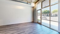 Located at 1400 S Figueroa Street in the heart of Los Angeles, this single-floor space combines modern design with industrial character. The open layout is anchored by durable wood-look flooring that runs throughout, while exposed concrete columns and visible ductwork overhead lend an authentic industrial aesthetic. Soaring ceilings amplify the sense of volume and openness across the main area.

Floor-to-ceiling glass storefront windows and double-door entries flood the interior with abundant natural light and offer clear sightlines to the surrounding streetscape, including mature trees and neighboring urban landmarks. The generous, unobstructed main area provides excellent flexibility for a variety of uses.

Toward the rear of the space, a well-appointed kitchen showcases contemporary dark wood cabinetry with sleek hardware, frosted glass upper cabinet accents, and a mosaic tile backsplash. Stainless steel appliances — including a gas range, microwave, dishwasher, and refrigerator — are complemented by light quartz countertops and a kitchen island, delivering both functionality and modern style. Additional partitioned rooms in the back offer space for private offices, storage, or support functions. The overall ambiance is clean, bright, and adaptable, making this a compelling urban space in a prime South Downtown Los Angeles location.