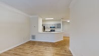 This single-floor residence features a clean, modern design characterized by light hardwood flooring, crisp white walls, and crown molding that runs throughout the main living areas. The open-concept layout connects the living area directly to the kitchen, which is defined by a peninsula counter with a built-in sink, offering both additional workspace and a natural division between the two areas. The kitchen is equipped with stainless steel appliances, including a refrigerator, range, and over-the-range microwave, complemented by gray cabinetry with brushed nickel hardware and white countertops. Ample upper and lower cabinet storage lines the kitchen walls, with a separate interior door providing additional access or storage.

The living area is generously proportioned, allowing flexible furniture arrangements, while the entry area benefits from a large window that invites natural light and outdoor views. The bedroom is well-sized, featuring a closet and a window overlooking what appears to be an exterior balcony or patio area. The bathroom includes a full soaking tub with white tile surround, a toilet, and a vanity area. Consistent hardwood-style flooring flows throughout, contributing to a cohesive and bright overall ambiance.
