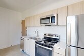 Located on Second Avenue in Detroit's vibrant Midtown district, this one-bedroom, one-bathroom unit offers a thoughtfully designed modern interior across a single floor. The open-plan living and dining area flows seamlessly from the kitchen, creating a bright, airy feel enhanced by large windows that invite abundant natural light and frame views of the surrounding neighborhood streetscape.

The kitchen is equipped with stainless steel appliances — including a refrigerator, electric range, built-in microwave, and dishwasher — paired with light wood cabinetry, clean white countertops, and a stainless steel sink. The minimalist aesthetic is consistent throughout, with crisp white walls and polished concrete-style flooring lending a contemporary industrial character to the space.

The bedroom is an intimate, well-defined room featuring a large picture window that offers expansive views of the tree-lined street below, filling the space with natural light. Two closets provide practical storage solutions within the unit.

The bathroom is finished with white subway tile in a walk-in shower stall, complemented by brushed nickel fixtures and clean, simple lines. A dedicated laundry area adds everyday convenience. Overall, the unit presents a clean, modern aesthetic well-suited to urban living in one of Detroit's most dynamic neighborhoods.