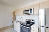 Located on Second Avenue in Detroit's vibrant Midtown district, this one-bedroom, one-bathroom unit offers a thoughtfully designed modern interior across a single floor. The open-plan living and dining area flows seamlessly from the kitchen, creating a bright, airy feel enhanced by large windows that invite abundant natural light and frame views of the surrounding neighborhood streetscape.

The kitchen is equipped with stainless steel appliances — including a refrigerator, electric range, built-in microwave, and dishwasher — paired with light wood cabinetry, clean white countertops, and a stainless steel sink. The minimalist aesthetic is consistent throughout, with crisp white walls and polished concrete-style flooring lending a contemporary industrial character to the space.

The bedroom is an intimate, well-defined room featuring a large picture window that offers expansive views of the tree-lined street below, filling the space with natural light. Two closets provide practical storage solutions within the unit.

The bathroom is finished with white subway tile in a walk-in shower stall, complemented by brushed nickel fixtures and clean, simple lines. A dedicated laundry area adds everyday convenience. Overall, the unit presents a clean, modern aesthetic well-suited to urban living in one of Detroit's most dynamic neighborhoods.