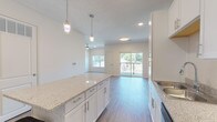 This well-appointed single-floor residence offers a clean, modern aesthetic throughout, with light-toned luxury vinyl plank flooring and a neutral color palette that creates a bright, welcoming atmosphere. The open-concept kitchen is a standout feature, showcasing white shaker-style cabinetry, granite countertops, and a central island with pendant lighting overhead. A full suite of stainless steel appliances — including a refrigerator, range, microwave, and dishwasher — provides a polished, functional cooking space. The kitchen flows seamlessly into the living area, which is spacious and filled with natural light from a sliding glass door that opens onto a private balcony with outdoor views. A ceiling fan keeps the living space comfortable year-round. The bedroom is generously sized, featuring a window that invites additional natural light, and connects directly to a well-designed bathroom. The bathroom includes a granite-topped vanity with white cabinetry, a glass-enclosed shower/tub combination, and the same consistent luxury vinyl plank flooring found throughout the residence. Recessed lighting and stylish fixtures complete the refined, contemporary feel of the space.