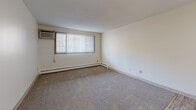Located at 153-155 Little Canada Rd E in Little Canada, MN, this one-bedroom, one-bathroom unit offers a functional and well-organized single-floor layout. The galley-style kitchen is lined with warm oak cabinetry on both sides, providing ample upper and lower storage. It is equipped with a white electric range, refrigerator, and a double-basin sink with light countertops, all set atop durable wood-look plank flooring. A pendant chandelier adds a subtle decorative touch to the kitchen/living area. The open living space features neutral carpet, a baseboard heating system, and a wall-mounted air conditioning unit, with vertical blinds on a large window that allows natural light to fill the room. The spacious bedroom also features plush carpet, baseboard heating, and a generous open closet with a full-width hanging rod for organized storage. A second closet is conveniently accessible off the kitchen. The bathroom includes a full tub and shower combination with clean white tile surround and chrome fixtures. Throughout the unit, neutral tones and textured ceilings create a cohesive, understated aesthetic suited for comfortable everyday living.