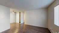 This single-floor residential unit offers a functional and clean layout with consistent dark hardwood-style flooring running throughout every room. The living area is open and well-proportioned, featuring a ceiling fan with light fixture, textured ceilings, and a large window that allows natural light to fill the space. A wall-mounted HVAC unit and baseboard heating provide climate control, and a front entry door opens directly into the living space.

The galley-style kitchen is efficiently designed with white shaker cabinetry, sleek bar-pull hardware, light quartz-style countertops, and white appliances including a range with oven, overhead exhaust hood, refrigerator, and a stainless steel double sink. Ample upper and lower cabinet storage maximizes the use of the compact kitchen footprint.

The bedroom is a well-sized, private room with a window offering natural light, textured ceilings, and access to a walk-in closet area. The bathroom features a full tub and shower combination with white tile surround, chrome fixtures, and a grab bar, maintaining a clean and utilitarian aesthetic. White walls and neutral tones throughout the unit create a bright, move-in-ready environment suitable for a range of furnishing styles.