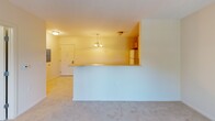 Located along East Lake Road in Erie, Pennsylvania, this single-floor unit offers a functional and well-organized layout designed for comfortable everyday living. The open-concept design connects the kitchen and living area seamlessly, creating a cohesive and practical living space. The kitchen is equipped with warm honey-toned wood cabinetry offering ample storage, light-colored countertops, and white appliances including a refrigerator, electric range, and over-the-range microwave. Tile flooring throughout the kitchen provides easy maintenance, while a breakfast bar peninsula separates the kitchen from the adjoining living area. The living area features neutral carpet flooring, light-toned walls, and is illuminated by a ceiling-mounted light fixture and a chandelier pendant near the entry. Natural light filters in through windows, enhancing the bright and airy atmosphere. The bedroom is carpeted with neutral tones and includes a window overlooking lush greenery, providing a calm and pleasant view. The full bathroom is finished with tile flooring, a vanity with a white countertop and integrated sink, a large mirror, and a glass-enclosed shower. Accessibility features include stainless steel grab bars near the toilet, making the space thoughtfully designed for a range of occupants.