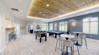 Located at 8501 Walther Blvd in Nottingham, Maryland, this single-story community amenity facility offers a thoughtfully designed collection of spaces for recreation, fitness, work, and social gathering. The standout game room features a striking wood-paneled tray ceiling with recessed and ambient lighting, slate-blue accent walls, and large windows that invite natural light. The room is furnished with a foosball table, pool table, and high-top seating, creating an engaging social environment. Adjacent to the game room is a comfortable lounge area with a fireplace framed by classic wainscoting, bold blue velvet accent chairs, and a wall-mounted television, offering a warm and inviting retreat. A private office space with double glass doors and hardwood flooring provides a quiet area for focused work, alongside a conference table seating area. The well-equipped kitchen features white shaker cabinetry, granite countertops, a subway tile backsplash, and stainless steel appliances. The expansive fitness center is divided into distinct zones, including a cardio area with treadmills, ellipticals, and stationary bikes set against a scenic mountain mural, a strength training area with free weights and cable machines, and a functional training zone stocked with medicine balls, resistance equipment, and floor-to-ceiling mirrors.