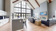 Located at 700 S Main St in Oshkosh, Wisconsin, this well-appointed single-floor community space offers a generous open layout designed for both gathering and relaxation. The architecture is immediately striking, with dramatically vaulted ceilings accented by rich, exposed wood beams that lend a warm yet contemporary character throughout the main living area.

The combined kitchen and living room serves as the heart of the space. The kitchen features white shaker cabinetry, granite countertops, stainless steel appliances, and a large island with bar seating — ideal for casual dining or entertaining. The adjacent living area centers around a stacked-stone fireplace with a wood mantel, flanked by comfortable seating and bathed in natural light from multiple windows.

A dedicated dining room provides flexible high-top table seating with warm leather swivel chairs, complemented by a billiards table and wall-mounted TV — creating a dynamic lounge atmosphere. A sliding barn door adds a stylish architectural detail to this area.

At the far end of the space, dramatic floor-to-ceiling glass curtain walls and French doors open directly to an outdoor pool area, flooding the interior with light and providing seamless indoor-outdoor connectivity. Light wood-look flooring runs throughout, tying each area together cohesively. The overall ambiance is modern, airy, and inviting.