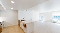 Located in Portland's vibrant NW District, this two-bedroom, two-bathroom residence offers a clean, modern aesthetic across a well-designed single-floor layout. The open-concept kitchen and living area serves as the heart of the home, anchored by a sleek white kitchen island with a black matte faucet and integrated sink. The kitchen is well-appointed with white shaker-style cabinetry, a tiled backsplash, stainless steel appliances including a full-size refrigerator and gas range, and recessed lighting throughout. Light wood-tone flooring extends seamlessly across all rooms, enhancing the bright and airy feel. The living area receives generous natural light through large windows and a glass door, with views of the surrounding urban environment. The primary bedroom is a comfortable retreat, featuring multiple windows, a dedicated bathroom with white cabinetry, quartz countertops, black hardware accents, and access to a walk-in closet with built-in shelving and hanging rods. The second bedroom is equally bright, with a well-positioned window that invites natural light. A second full bathroom serves the additional bedroom. The overall design is characterized by a crisp white palette, contemporary fixtures, and a cohesive, minimalist sensibility throughout.