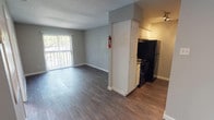 This efficient single-story, one-bedroom, one-bathroom residence is thoughtfully designed to maximize functionality within a compact footprint. Dark hardwood-style flooring runs consistently throughout the unit, lending a cohesive and contemporary feel to the entire space.

The open living area is bright and welcoming, featuring a sliding glass door with vertical blinds that fills the room with natural light and provides direct access to an outdoor area. A white front entry door and neutral gray walls give the space a clean, understated aesthetic.

The galley-style kitchen is positioned just off the main living area and is equipped with white cabinetry, speckled gray countertops, a double sink, and black appliances including a range and refrigerator. The efficient corridor layout makes practical use of the available space.

The bedroom is well-proportioned and benefits from a window fitted with horizontal blinds, allowing for natural light and privacy control. A ceiling fan with a built-in light fixture provides both ventilation and overhead illumination.

The bathroom features a vanity with white cabinetry, a speckled gray countertop, an integrated sink, and a large wall mirror with overhead lighting. The bathroom connects directly to the bedroom, offering a convenient layout. Throughout the unit, clean lines and neutral tones create a functional and move-in-ready living environment.