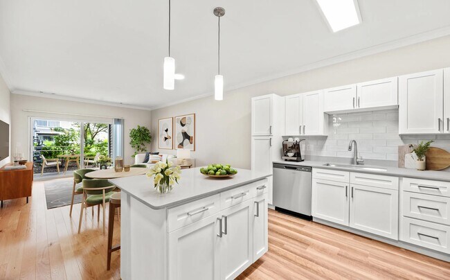 Cocina de concepto abierto con gabinetes estilo Shaker, una espaciosa isla de preparación y una perfecta integración con las áreas de comedor y sala de estar para una vida cotidiana más cómoda. - The Avens at Dedham Station