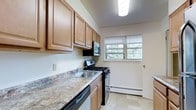 This single-floor space offers a thoughtfully designed layout centered around a functional and inviting kitchen. The kitchen is outfitted with warm honey-toned wood cabinetry that provides ample storage, complemented by granite-style countertops that add a touch of elegance to the space. Stainless steel appliances, including a gas range, built-in microwave, and dishwasher, lend a modern and practical edge to the cooking area. A double-basin sink sits beneath the countertop, making meal prep and cleanup convenient. Light tile flooring runs throughout the kitchen, contributing to a clean and bright aesthetic. A window above the range area allows natural light to filter in, offering a pleasant view of the surrounding greenery and creating an airy atmosphere. A baseboard heating unit ensures year-round comfort. The overall ambiance of the space is warm and practical, with a layout that maximizes utility while maintaining a welcoming feel. The combination of classic wood finishes, durable surfaces, and natural light makes this a comfortable and efficient living environment well-suited for everyday use.