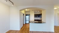 This single-floor residence offers a thoughtfully designed layout that balances functionality and comfort throughout. The kitchen serves as a central highlight, showcasing rich dark cabinetry, dark granite countertops, and a full suite of stainless steel appliances including a refrigerator, electric range, and over-the-range microwave. A tiled backsplash adds texture and depth to the cooking area, while track lighting overhead ensures excellent visibility. The kitchen flows seamlessly into the living area via a curved peninsula breakfast bar, framed by a striking arched passageway that adds architectural character to the open-concept design. Warm hardwood-style flooring extends throughout the main living and kitchen areas, contributing to a cohesive and inviting atmosphere. The living area benefits from natural light streaming through a glass-paned door that opens to a balcony, complemented by a ceiling fan for year-round comfort. The bedrooms are carpeted for added warmth and comfort, each featuring ceiling fans and windows with exterior views. The space also includes a utility area with an electrical panel. Overall, the residence presents a clean, neutral palette with practical finishes and a well-connected floor plan suited for everyday living.