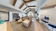 Located at 8009 Cameryn Pl in Pasadena, Maryland, this single-story community clubhouse offers a well-appointed gathering space spanning a generous floor area. The interior is anchored by a dramatic great room featuring soaring vaulted ceilings adorned with rich wood beam accents, wide-plank hardwood flooring, and an abundance of recessed lighting. Comfortable sectional seating, a dedicated billiards table, and a shuffleboard table make this lounge ideal for socializing and recreation, while large windows flood the space with natural light. A stylish refreshment bar area offers a granite-topped island with bar seating, white cabinetry, subway tile backsplash, stainless steel appliances, and decorative pendant lighting — perfect for hosting community gatherings. A utility prep area with granite countertops, a stainless sink, and classic wainscoting provides additional functional support. The fitness center is split across two well-lit rooms equipped with treadmills, ellipticals, weight machines, free weights, and benches. Outside, a large rectangular swimming pool is surrounded by a spacious patio deck with lounge chairs, shaded seating areas, and mature trees providing a tranquil, private setting under open skies.