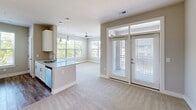 Located at 8010 Mosaic Drive in Charlotte, NC, this single-floor residence offers three bedrooms and two bathrooms within a thoughtfully designed floor plan. The open-concept living and kitchen area serves as the heart of the home, where a granite-topped peninsula with a undermount sink and pendant lighting creates a natural divide between cooking and living spaces. The kitchen is equipped with stainless steel appliances, a subway tile backsplash, and crisp white cabinetry with brushed nickel hardware, complemented by wood-look flooring. The living area extends toward a set of glass French doors with transom windows above, filling the space with natural light. Plush carpeting flows throughout the bedrooms, each fitted with ceiling fans and windows dressed with horizontal blinds offering outdoor views. The generously sized primary bedroom includes an en-suite bathroom featuring a dual-sink granite vanity with white cabinetry and wood-look flooring. The second bathroom mirrors similar finishes, offering a granite vanity and a tub-shower combination. Neutral warm-toned walls and clean white trim carry throughout, creating a cohesive and modern aesthetic across the entire residence.