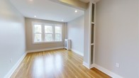 This 1-bedroom, 1-bathroom unit offers a clean, modern aesthetic across a single level. The living area is highlighted by warm hardwood flooring that runs throughout, complementing the neutral, light-toned walls that create a bright and welcoming atmosphere. Recessed lighting is installed in the ceiling, providing even, ambient illumination that enhances the sense of openness. A set of double-hung windows allows natural light to pour in, offering views of the surrounding greenery outside. Crisp white baseboards and trim provide a polished contrast to the warm tones of the floors. A distinctive architectural column with built-in decorative shelving adds a unique design element, offering both character and functional display space. The unit also features a compact heating unit tucked neatly into the space, maintaining the clean lines of the room. The overall ambiance is calm and refined, with thoughtful details that balance practicality and style. The neutral palette and quality finishes make this a versatile space well-suited for a variety of living arrangements.