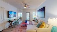 Located in Santa Rosa Beach, Florida, this single-floor residence captures the relaxed elegance of coastal living through thoughtfully designed interiors and beach-inspired décor throughout. The open-concept living area is bright and welcoming, featuring crown molding, wood-look flooring, a ceiling fan, and large windows and glass doors that invite ample natural light. A comfortable sectional sofa, bold patterned area rug, and vibrant accent pieces create a lively yet relaxed atmosphere, complemented by a wall-mounted TV and a dedicated workspace with a writing desk. The dining area makes a striking impression with a full-wall beach boardwalk mural, a round white dining table, and tufted aqua chairs beneath track lighting — a standout design feature that sets a coastal tone. The galley-style kitchen is equipped with stainless steel appliances, light cabinetry, and stone-look countertops, with access to a dedicated laundry area. The bedrooms offer restful retreats: one features a chevron wood headboard and beach artwork, while another showcases a tufted upholstered headboard set against a soft striped accent wall. The bathroom includes a dual-sink vanity with tile flooring. Throughout the space, a consistent coastal color palette of aqua, white, and sandy tones ties every room together harmoniously.