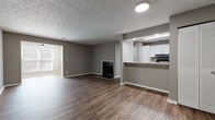This single-floor residence offers a cohesive and functional layout designed for comfortable everyday living. The open-concept living and dining area serves as the heart of the home, featuring rich dark hardwood-style flooring, neutral gray walls, and a textured ceiling that adds visual depth. A classic fireplace anchors the living space, providing a warm focal point, while natural light filters in through windows fitted with blinds. A half-wall partition seamlessly connects the living area to the kitchen, maintaining an airy, open feel. The kitchen is well-equipped with black appliances, including a range, refrigerator, and dishwasher, complemented by crisp white cabinetry, a mosaic tile backsplash, and light granite-style countertops. The dark hardwood-style flooring continues throughout the kitchen, tying the main living spaces together. The bedrooms offer plush wall-to-wall carpeting, neutral tones, and natural light from windows, creating restful and inviting retreats. The bathroom is appointed with a white vanity featuring granite-style countertops, a tub-shower combination, and matching hardwood-style flooring, maintaining the consistent aesthetic found throughout the home. Clean white trim and baseboards provide a polished finishing touch across every room.
