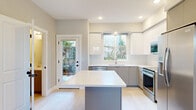 This thoughtfully designed two-story home offers a clean, contemporary aesthetic across two well-proportioned floors. The main level features an open-concept layout where the kitchen and living areas flow seamlessly together. The kitchen is a standout, showcasing two-tone cabinetry with gloss white upper cabinets and gray lower cabinets, a classic white subway tile backsplash, quartz countertops, stainless steel appliances including a French door refrigerator and range, and a central island with additional prep space. Natural light pours in through multiple windows, including a garden-facing window above the sink and a glass door providing direct outdoor access. The living room is anchored by a tile-surround fireplace with a clean white mantle and is equipped with a wall-mounted mini-split unit for efficient climate control. Light hardwood flooring runs throughout the main level, lending a bright, airy feel. Upstairs, the spacious primary bedroom features plush carpet, a mini-split unit, and ample closet space with built-in shelving. The second bedroom offers a scenic outdoor view. Three bathrooms are finished with marble-style tile flooring, gray vanities, white quartz countertops, and full tub-shower combinations, maintaining a consistent, modern style throughout.