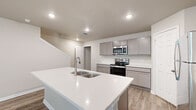 This two-story home is thoughtfully laid out across two floors, with the more compact main level dedicated to shared living spaces and the larger upper floor accommodating the majority of the private rooms. The main level features an open-concept kitchen and living area finished with wood-look plank flooring and recessed lighting throughout. The kitchen is a standout feature, centered around a substantial island with a white quartz countertop and an undermount double sink. Grey shaker-style cabinetry lines the walls, complemented by stainless steel appliances including a range, microwave, and refrigerator. A pantry provides additional storage nearby. The attached garage includes a water heater and direct interior access. Upstairs, five bedrooms offer natural light through windowed walls with blinds and neutral-toned walls. The primary bedroom includes an en-suite bathroom with a dual-sink vanity featuring grey cabinetry and a large mirror, as well as a dedicated walk-in closet with built-in shelving and hanging rods. A dedicated laundry room with full-size washer and dryer hookups and overhead shelving adds convenience. The fenced backyard provides a private outdoor retreat with mature trees and green lawn.