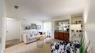 This single-story residence offers a thoughtfully designed layout that balances comfort and functionality across its key living spaces. The living room serves as the heart of the home, featuring plush carpeting, a textured ceiling, and a large sliding glass door that fills the space with natural light. A standout feature is the built-in wet bar with warm wood cabinetry, a stone-style countertop, and glass shelving — an ideal setup for entertaining. Adjacent open shelving adds additional display and storage options.

The galley-style kitchen is efficiently arranged with rich wood cabinetry lining both walls, ample counter space, a double-basin sink, and full suite of white appliances including a stove, refrigerator, and microwave. Wood-look flooring adds a warm contrast to the cabinetry.

The dedicated dining area provides a defined space for meals, accommodating a full-sized dining table with ease. The bedroom is a calm retreat, complete with carpet flooring, a ceiling fan with light fixture, a window for natural light, and direct access to a generously sized walk-in closet outfitted with dual hanging rods and built-in shelving. The bathroom features a wide vanity with a stone-look countertop and a large mirror, offering a clean and practical design throughout.