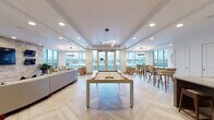 Located at 455 E 400 S in Salt Lake City, Utah, this contemporary amenity lounge is designed to impress with a refined blend of modern finishes and welcoming social spaces. Throughout the space, light herringbone-patterned hardwood flooring unifies each distinct zone, while recessed lighting and designer pendant fixtures create a warm, polished atmosphere.

The main lounge area anchors the space with a full-size billiards table positioned beneath a striking geometric chandelier. Floor-to-ceiling windows and glass doors flood the room with natural light and provide direct access to an outdoor terrace. A bar-height seating area along the windows offers views of the surroundings, ideal for casual gatherings.

A dedicated lounge nook features plush seating arranged beneath a circular wood-toned pendant light, with corner glass walls framing outdoor courtyard views. Nearby, a casual dining area with a glass-top bistro table and accent chairs is accented by vibrant artwork and additional terrace-facing windows.

The fully equipped kitchen is a standout feature, showcasing granite countertops, a large island with bar seating, stainless steel appliances including a professional range, and a natural stone tile backsplash. Adjacent to the kitchen, a media lounge offers a curved sectional sofa and multiple wall-mounted screens set against a textured stone accent wall, perfect for sports viewing or relaxed entertainment.