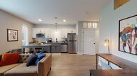 Located at 750 E Broad St in Columbus, Ohio, this single-floor unit offers a thoughtfully designed open-concept layout that seamlessly connects the kitchen, dining, and living areas. The kitchen is a standout feature, showcasing two-toned cabinetry with crisp white upper cabinets and slate gray lower cabinets, a white subway tile backsplash, quartz countertops, stainless steel appliances including a refrigerator, dishwasher, and range, and stylish pendant lighting overhead. A dining table with bar seating sits adjacent to the kitchen, making the space ideal for both casual meals and entertaining. The living area is bright and welcoming, with large windows that invite natural light and feature wood-look flooring underfoot. The bedroom is a calm retreat finished with soft carpet, neutral tones, and ample space. The bathroom offers a clean, modern aesthetic with deep teal accent walls, a glass-enclosed walk-in shower, and matte black hardware throughout. A hallway laundry closet with a stacked washer and dryer unit adds everyday convenience. The overall design balances contemporary finishes with a warm, livable atmosphere throughout.