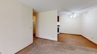 Located at 801 County Road D E in Vadnais Heights, Minnesota, this single-floor unit offers a practical and comfortable layout. The living area is generously sized, featuring plush wall-to-wall carpeting, a ceiling fan, baseboard heating, and a wall-mounted air conditioning unit. A sliding glass door with vertical blinds fills the space with natural light and provides outdoor access. The open layout connects the living area to the kitchen, which is appointed with dark wood cabinetry offering ample storage, a white electric range, a refrigerator, a single-basin sink, and hardwood-style flooring that adds warmth to the space. A closet at the end of the kitchen provides additional storage convenience. The bedroom is carpeted and features a ceiling fan, a window with blinds for natural light, and baseboard heating. The full bathroom is clean and functional, outfitted with a single-sink vanity with wood cabinetry, a tiled tub-shower combination, a large mirror, and classic mosaic tile flooring. Throughout the unit, neutral wall tones and clean finishes create a simple, move-in-ready atmosphere well-suited for everyday living.