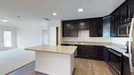 This single-story residence offers two bedrooms and two bathrooms with a cohesive design throughout. The kitchen is a standout feature, showcasing rich dark espresso-toned shaker cabinetry that extends floor to ceiling, providing generous storage. Light granite-style countertops contrast the dark cabinets, while stainless steel appliances—including a range, over-the-range microwave, and refrigerator—complete the functional layout. A kitchen island with matching countertop adds additional workspace and enhances the open flow toward the living area.

The living area is carpeted in neutral tones and features crown molding, with access to an outdoor space through glass doors that allow natural light to fill the room. Both bedrooms are carpeted and receive natural light through sizable windows. One bedroom includes a spacious walk-in closet fitted with wire shelving systems, offering practical storage solutions.

Each bathroom mirrors the kitchen's design aesthetic, featuring dark vanity cabinetry, white countertops, and classic black-and-white mosaic tile flooring. Both bathrooms include tub-shower combinations with full surround tile. The consistent use of dark cabinetry against white surfaces gives the residence a clean, contemporary character throughout.