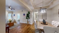 This thoughtfully designed 2-bedroom, 2-bathroom single-floor residence offers a comfortable and cohesive living experience. Warm hardwood-style flooring flows throughout the main living areas, anchoring an open-concept layout that connects the living room, dining area, and hallway seamlessly. The living room features crown molding, a ceiling fan, and built-in shelving, with natural light streaming in through large windows and a sliding glass door. An elegant drum pendant light distinguishes the dining area, which also benefits from natural light through slatted blinds. The kitchen connects conveniently to the dining space for easy entertaining.

Both bedrooms are carpeted for comfort and include ceiling fans, generous windows with outdoor views, and ample closet storage. The primary bedroom offers a well-sized layout, while the second bedroom provides comparable comfort. The bathrooms include one with a dual-sink vanity featuring dark cabinetry, a large mirror, and a shower-tub combination. A dedicated laundry room houses a full-sized washer and dryer with additional shelving overhead. The hallway ties all areas together efficiently, making the layout practical and easy to navigate. Overall, the space presents a warm, neutral aesthetic throughout.