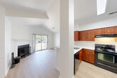 Located at 630 Smithfield Road in North Providence, Rhode Island, this one-bedroom, one-bathroom unit offers a well-designed single-floor layout with a bright, open feel throughout. The living room is a standout space, featuring soaring vaulted ceilings, light hardwood-style flooring, and a fireplace. Sliding glass doors lead to a private balcony with outdoor views of the surrounding community and green landscape. The kitchen is thoughtfully designed with warm cherry wood cabinetry, white countertops, a stainless steel sink, and black appliances including a refrigerator, range, dishwasher, and built-in microwave hood. A pass-through connects the kitchen to the main living area, enhancing the open-concept flow. The bedroom is carpeted and features vaulted ceilings, a window allowing natural light, and access to a dedicated walk-in closet. The bathroom includes a full tub-shower combination with clean white finishes. Additional conveniences include a hallway, a dedicated laundry area, and ample closet storage. The unit's vaulted ceilings and white walls create an airy, spacious ambiance throughout, making efficient use of the overall floor area.
