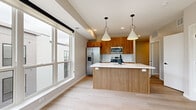 This single-floor residence showcases a thoughtfully designed open-concept layout with clean, contemporary finishes throughout. The kitchen serves as a central highlight, featuring warm-toned wood cabinetry that extends to the upper walls, contrasted by crisp white quartz countertops and a classic white subway tile backsplash. A spacious kitchen island with an undermount sink and matte black faucet provides additional prep space and casual seating opportunities. Stainless steel appliances, including a French door refrigerator, electric range, built-in microwave, and dishwasher, complete the well-equipped cooking area. Geometric pendant lights hang above the island, adding a modern design accent.

Light-toned hardwood flooring runs continuously throughout the unit, enhancing the sense of openness and cohesion. The living and sleeping areas are bright and airy, benefiting from large windows that frame views of the surrounding neighborhood's tree-lined streets and adjacent buildings. One area features direct access to a balcony with black metal railing, offering a seamless indoor-outdoor connection. Neutral warm-white walls throughout the unit maintain a calm, inviting ambiance suited to a variety of interior styles.