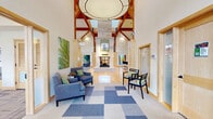 This well-appointed clubhouse in Loveland, Colorado offers a generous single-floor layout thoughtfully designed for community gathering and recreation. The centerpiece is a grand main lounge showcasing soaring vaulted ceilings with exposed wood beams, warm hardwood flooring, and an impressive stone fireplace. Floor-to-ceiling windows and clerestory glazing flood the space with natural light, while French doors open directly to an outdoor patio area. A dedicated game room features a full-size pool table, foosball, an arcade cabinet, dartboard, and comfortable seating beneath high ceilings, creating an energetic social hub. The private theater room is equipped with tiered seating — including plush recliners and lounge sofas — a ceiling-mounted projector, and a large projection screen framed by acoustic wall panels for an immersive viewing experience. A café-style lounge provides a beverage station, dining tables, and wall-mounted TV, ideal for casual gatherings. The conference room offers a long boardroom table surrounded by upholstered chairs beneath a statement pendant light, accented by colorful artwork and generous natural light. Throughout, patterned carpeting, warm wood trim, and a cohesive modern palette tie the spaces together into a versatile and inviting community destination.