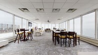 Located in Lakewood, Ohio, this elevated single-floor gathering space offers a striking combination of open-concept design and breathtaking panoramic views of Lake Erie and the Cleveland skyline. Floor-to-ceiling windows wrap around the perimeter, flooding the interior with natural light and framing sweeping waterfront vistas from nearly every vantage point.

The main lounge area features a generously sized sectional sofa accented with yellow and patterned throw pillows, complemented by sleek arc floor lamps and a wall-mounted flat-screen TV. The space transitions seamlessly into multiple dining zones, furnished with dark wood high-top tables and counter-height chairs with yellow upholstered seats, providing versatile seating configurations ideal for events or gatherings.

A dedicated kitchen area supports the space with full appliances including a stainless steel refrigerator, range, microwave, and ample cabinetry with frosted glass upper doors and a classic subway tile backsplash. A second kitchenette or bar area features white cabinetry with quartz-style countertops, a second full-size refrigerator, and its own stunning lake view through large windows.

Underfoot, a textured patterned carpet grounds the lounge and dining areas, while light-toned tile flooring defines the kitchen spaces. The drop ceiling with recessed lighting and ceiling fans ensures a comfortable, well-lit environment throughout.