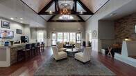 This single-floor amenity and clubhouse space combines sophisticated design with a welcoming, community-focused atmosphere. The centerpiece is a grand main lounge featuring soaring vaulted ceilings with striking dark wood beam accents and shiplap detailing, anchored by a statement chandelier that draws the eye upward. Rich hardwood flooring runs throughout, adding warmth and continuity across the space.

The main lounge area is thoughtfully furnished with accent chairs, plush seating, and a large area rug, creating an inviting gathering space. Large floor-to-ceiling windows and glass doors line the rear wall, flooding the interior with natural light and offering direct views of the outdoor pool and surrounding greenery. A cozy banquette nook, accented by exposed brick and wood-paneled walls, provides a more intimate setting complete with a wall-mounted television.

A well-appointed kitchenette/bar area features granite countertops, dark cabinetry, a sink, under-counter refrigeration, and a coffee station, making it ideal for social gatherings. Adjacent bar-height seating at granite-topped islands adds to the communal feel. A dedicated study room offers built-in granite desks and office chairs for focused work. The entry corridor features wainscoting and decorative details that set an elegant tone from arrival.
