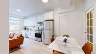 This single-floor residence offers five private bedrooms, one full bathroom, a kitchen, and a hallway, all finished with a clean, modern aesthetic. The open-concept kitchen and living area serves as the heart of the home, featuring white shaker-style cabinetry extending to the ceiling, stainless steel appliances including a gas range, built-in microwave, dishwasher, and full-size refrigerator, complemented by a marble-look countertop. Light wood-look flooring flows throughout the entire unit, enhancing the bright, airy atmosphere created by white walls and recessed lighting. The living area accommodates comfortable seating and dining, with natural light streaming in through multiple windows. Each of the five bedrooms is compact yet functional, outfitted with light hardwood flooring, large windows that invite natural light and outdoor views, and individual storage solutions including wardrobes. The bedrooms maintain a consistent minimalist design with crisp white walls. The shared bathroom is finished with a clean white tub-shower combo accented by matte black fixtures, maintaining the modern design language found throughout the residence. A hallway connects the rooms, contributing to an efficient and practical layout.