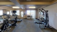 Located at 3304 E 44th Ave in Spokane, Washington, this single-floor fitness center is a well-equipped exercise facility designed to support a full range of workout routines. The space features a thoughtfully arranged selection of cardio equipment, including treadmills, elliptical trainers, and stationary bikes, providing ample options for aerobic exercise. A multi-station strength machine, weight bench, and stability balls round out the strength and flexibility offerings.

The room is finished with durable, patterned carpet tiles and warm neutral-toned walls, creating a functional and welcoming environment. A large wall-mounted mirror extends along one side, enhancing the sense of space and allowing users to monitor their form during workouts. Recessed ceiling panels with flush lighting provide consistent, even illumination throughout the room.

A wall-mounted flat-screen television is positioned for easy viewing from the cardio area. Hand sanitizer dispensers are conveniently placed near the entrance. The fitness center benefits from abundant natural light, courtesy of multiple windows and a full glass sliding door fitted with vertical blinds that opens directly onto an outdoor balcony. The balcony overlooks the surrounding Spokane landscape, offering a refreshing outdoor connection to complement the indoor workout experience.