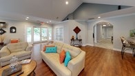 Located at 700 Greenlawn Dr in Columbia, SC, this single-floor community gathering space combines comfort and style with a thoughtfully designed open layout. Rich hardwood flooring flows throughout, unifying each area seamlessly.

The main living area is an immediate focal point, anchored by a striking floor-to-ceiling stacked stone fireplace fitted with a mounted flat-screen television and framed by elegant white columns. Vaulted ceilings with recessed lighting enhance the sense of openness, while French doors along one wall invite natural light and provide direct access to the outdoor area. Multiple seating arrangements — including a cream sofa with vibrant accent pillows and patterned armchairs — create a comfortable, social atmosphere.

Adjacent to the living area, the dining space features warm, neutral tones, crown molding, and large windows overlooking lush greenery, offering a bright and pleasant setting for gatherings. A round glass-top dining table with upholstered chairs accommodates small groups in an intimate setting.

The kitchen is well-appointed with dark espresso cabinetry, granite countertops, stainless steel appliances, a subway tile backsplash, and a peninsula breakfast bar with seating — ideal for casual dining or entertaining. Crown molding throughout adds a refined finishing touch, making this a polished and functional space suited for community events and social gatherings alike.