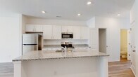 Located at 2108 Silty Soil Ct in Leland, NC, this two-story home offers four bedrooms, two full bathrooms, and a well-organized layout spread across two floors. The main level features an open-concept kitchen equipped with white shaker-style cabinetry, granite-look countertops, stainless steel appliances including a refrigerator, range, and microwave, and a peninsula island with an integrated sink — ideal for both meal prep and casual dining. Recessed lighting and warm wood-look flooring flow throughout the main living areas, complemented by a ceiling fan in the living space and sliding glass doors that bring in natural light and outdoor access. The bathrooms are finished with granite-topped vanities, white cabinetry, and tub-shower combinations with clean white surrounds. The generously sized primary bedroom includes a walk-in closet with wire shelving for organized storage. Additional bedrooms feature wood-look flooring and windows that let in natural light. Three closets are distributed throughout the home for ample storage. The attached garage includes an automatic opener, a concrete floor, and direct interior access, providing both parking and additional utility space.