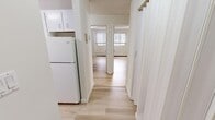 This 2-bedroom, 1-bathroom unit in Calgary, AB offers a clean, functional layout with consistent light hardwood flooring running throughout the space. The entrance leads into a central hallway connecting all areas of the home, with the kitchen positioned conveniently nearby. The kitchen features white cabinetry — both upper and lower — a subway tile backsplash, white countertops, and white appliances including an electric range and refrigerator, providing ample storage and prep space. The combined living room area is generously sized, featuring a textured ceiling, baseboard heating, and large windows with balcony access that bring in natural light and views of the surrounding greenery and neighbourhood. Both bedrooms are bright and well-proportioned, each with windows fitted with blinds for privacy, light hardwood floors, textured ceilings, and baseboard heating. The bathroom includes a full tub and shower combo with warm-toned ceramic tile surround, a toilet, and a vanity with mirror. Throughout the unit, the neutral white and warm wood tones create a clean, cohesive aesthetic that is easy to personalize.