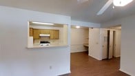 Located at 100 Chapelridge Dr in Richland, Mississippi, this single-story unit offers a functional and straightforward layout designed for everyday living. The open-concept design connects the main living area to the kitchen via a pass-through window, creating a sense of connectivity between the two spaces. The kitchen is equipped with warm-toned oak cabinetry, a white electric range with an overhead ventilation hood, and light-colored countertops. Fluorescent lighting illuminates the kitchen workspace efficiently.

The main living area features hardwood-style flooring that extends throughout the unit, adding warmth and visual continuity. White walls and a textured ceiling keep the interior feeling clean and cohesive. Toward the back of the unit, an additional room offers built-in shelving and a built-in desk or workspace surface, making it suitable for use as a home office or study area. A separate door provides access to additional storage or a utility space.

The overall ambiance is practical and neutral, offering a blank canvas that can be easily personalized. The single-floor layout ensures convenient, step-free living throughout the entire space.