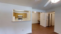 Located at 100 Chapelridge Dr in Richland, Mississippi, this single-story unit offers a functional and straightforward layout designed for everyday living. The open-concept design connects the main living area to the kitchen via a pass-through window, creating a sense of connectivity between the two spaces. The kitchen is equipped with warm-toned oak cabinetry, a white electric range with an overhead ventilation hood, and light-colored countertops. Fluorescent lighting illuminates the kitchen workspace efficiently.

The main living area features hardwood-style flooring that extends throughout the unit, adding warmth and visual continuity. White walls and a textured ceiling keep the interior feeling clean and cohesive. Toward the back of the unit, an additional room offers built-in shelving and a built-in desk or workspace surface, making it suitable for use as a home office or study area. A separate door provides access to additional storage or a utility space.

The overall ambiance is practical and neutral, offering a blank canvas that can be easily personalized. The single-floor layout ensures convenient, step-free living throughout the entire space.